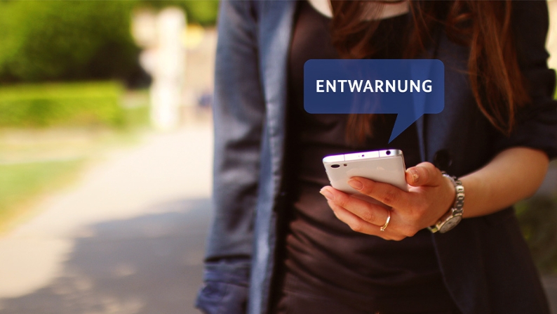 Symbolbild einer erhaltenen Cell Broadcast-Entwarnung auf den Smartphone einer Passantin